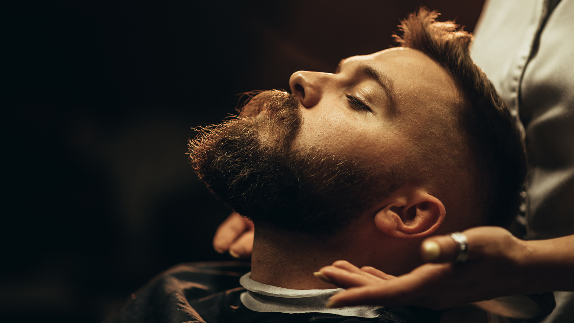 Close shot of a young man beard while he is sitting at a barbershop