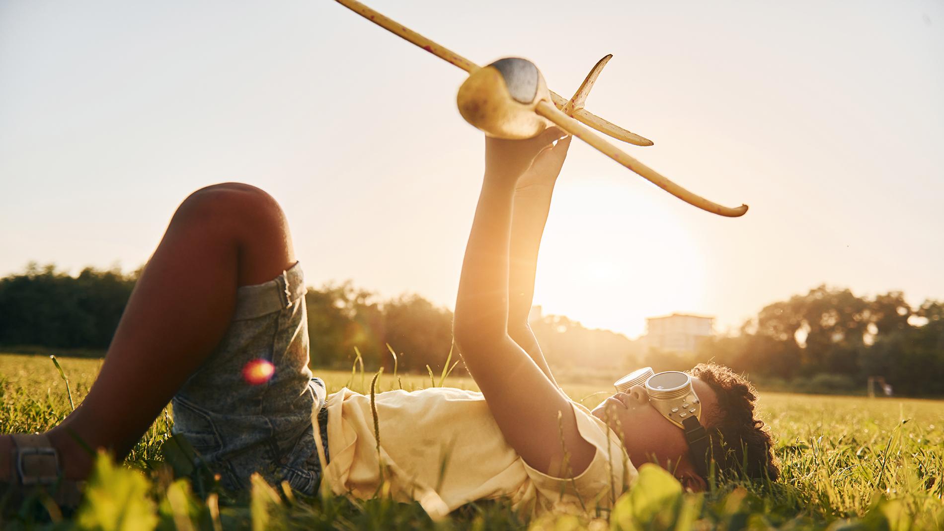 In glasses with toy plane. African american kid have fun in the field at summer daytime